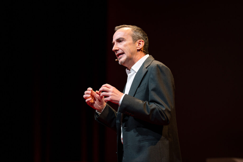 Ein Speaker gestikuliert mit beiden Händen auf der TEDxBruneck-Bühne